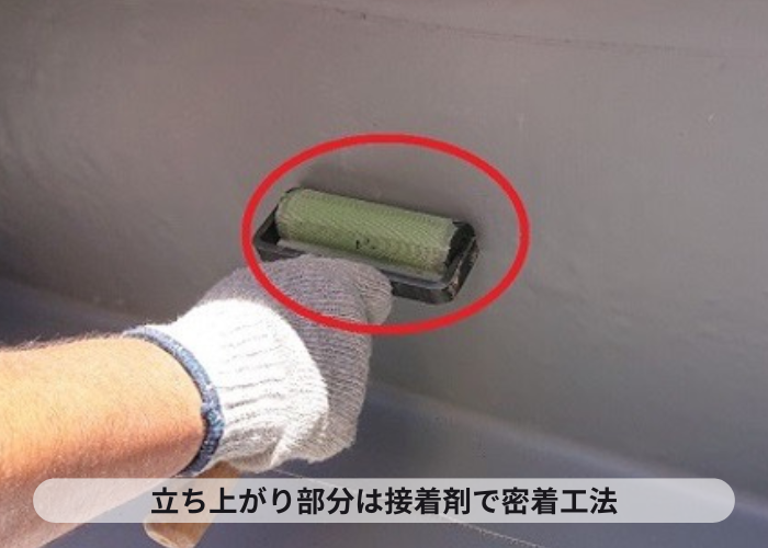 尼崎市　陸屋根防水工事で立ち上がり部分に塩ビシートを貼っている様子